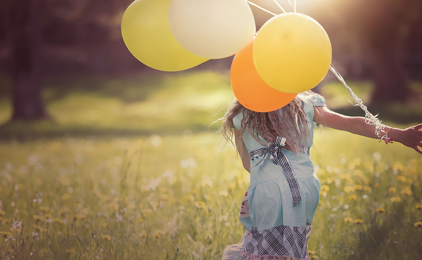 woman running through field holding balloons